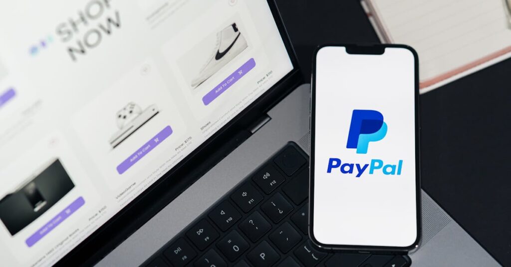 pexels-photo-29502367-29502367-1 Smartphone displaying PayPal logo next to laptop with online shopping site open.