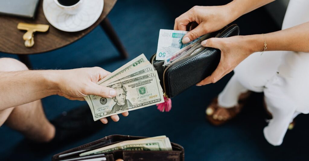 Close-up of two people exchanging US dollars and currency with wallets on a table.