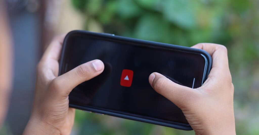 Close-up of hands holding a smartphone displaying a video app icon outdoors.